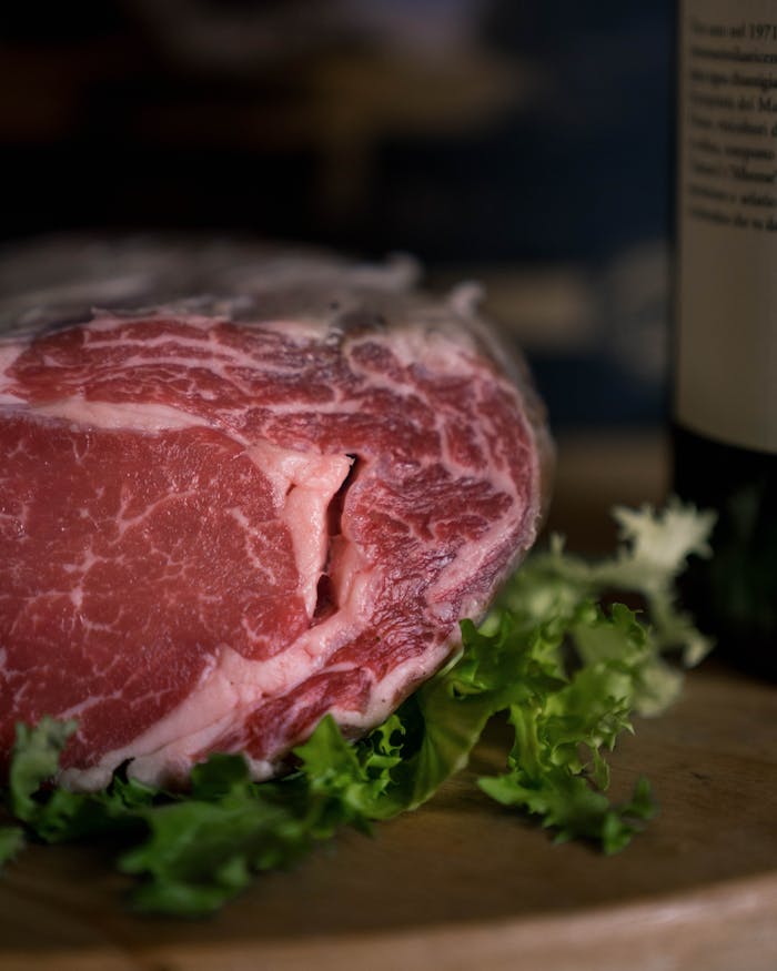 Close-up of a raw beef steak on a cutting board surrounded by fresh lettuce.