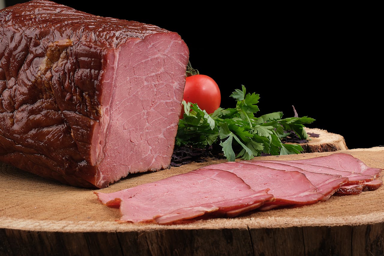 About Close-up of sliced roast beef on wooden board garnished with fresh parsley and tomato, highlighting rich texture.