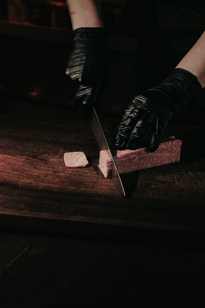 About Close-up of a chef's hands slicing Wagyu beef on a wooden board.