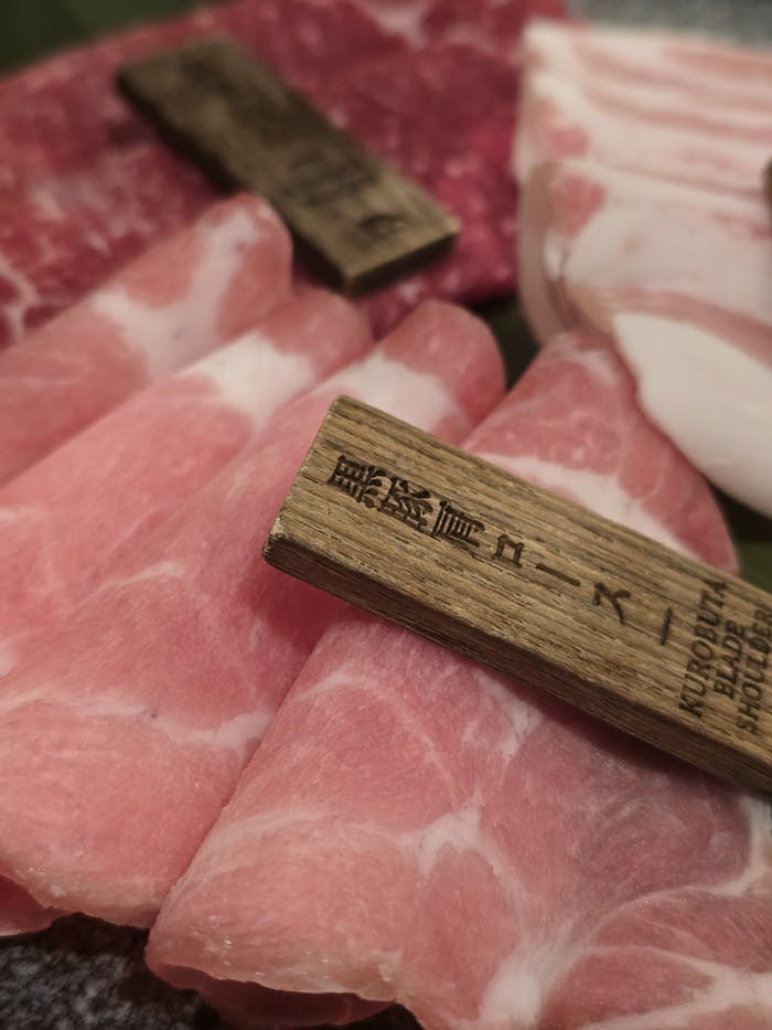 Close-up of thinly sliced pork with wooden tags showcasing Kuropata cut detail.